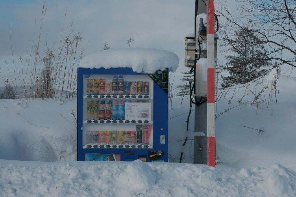 A vending machine covered in snow, surrounded by a serene winter landscape.